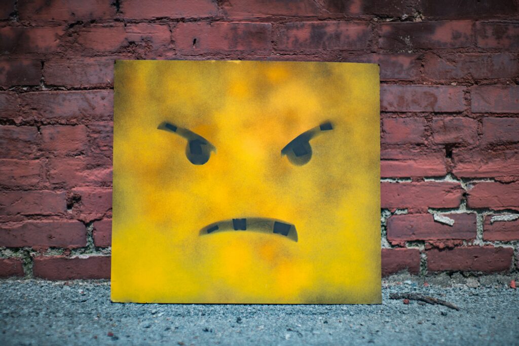 Yellow canvas with frowning face rests against brick wall