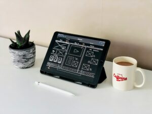 iPad displaying UX designs beside coffee mug and plant